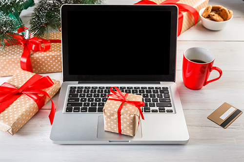 Christmas online shopping. Laptop with copy space on screen lay on white wood, present boxes and christmas tree on background. Internet commerce on winter holidays concept