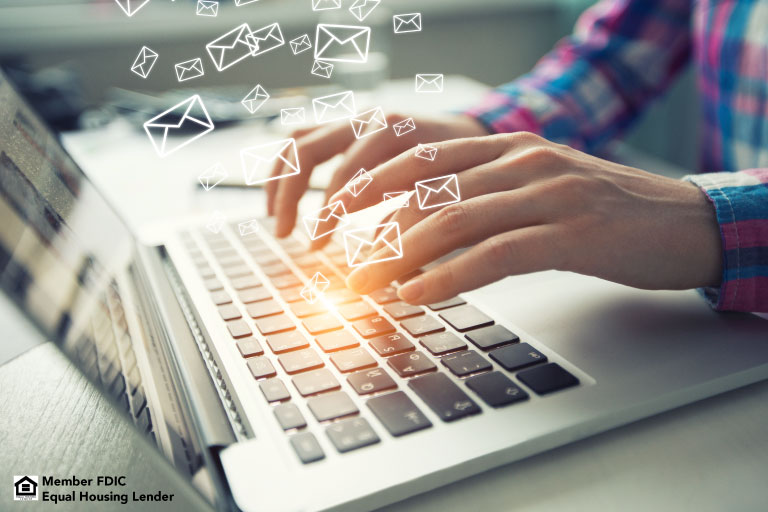Person typing on computer. Numerous email icons appear above and around the keyboard in a way that represents many emails being sent and received.