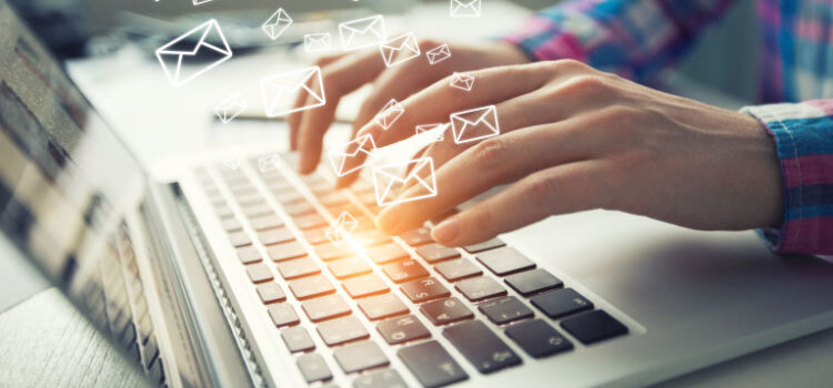 Person typing on computer. Numerous email icons appear above and around the keyboard in a way that represents many emails being sent and received.
